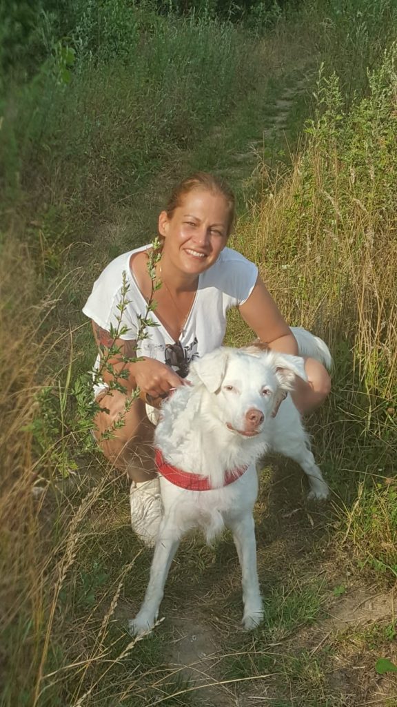 Stephanie Labes die Hundephysiotherapeutin steht in Duisburg mit Hund auf Rasen und lächelt in die Kamera. 